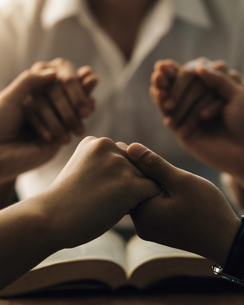 Människor som håller varandras händer i bön över en uppslagen bibel